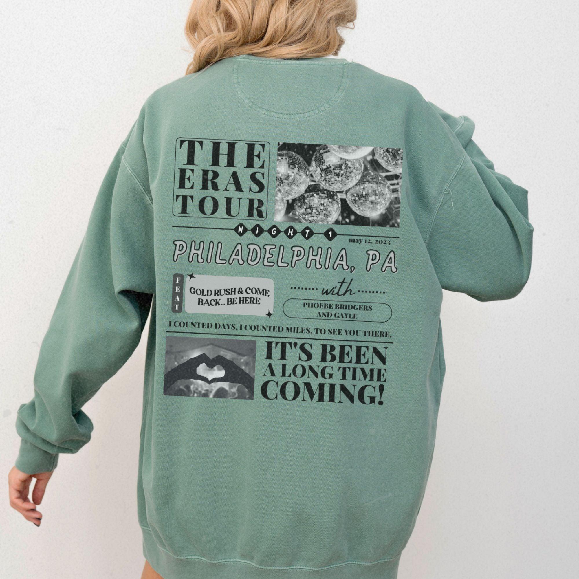 a woman wearing a green sweatshirt with the words the eras tour philadelphia pa on it