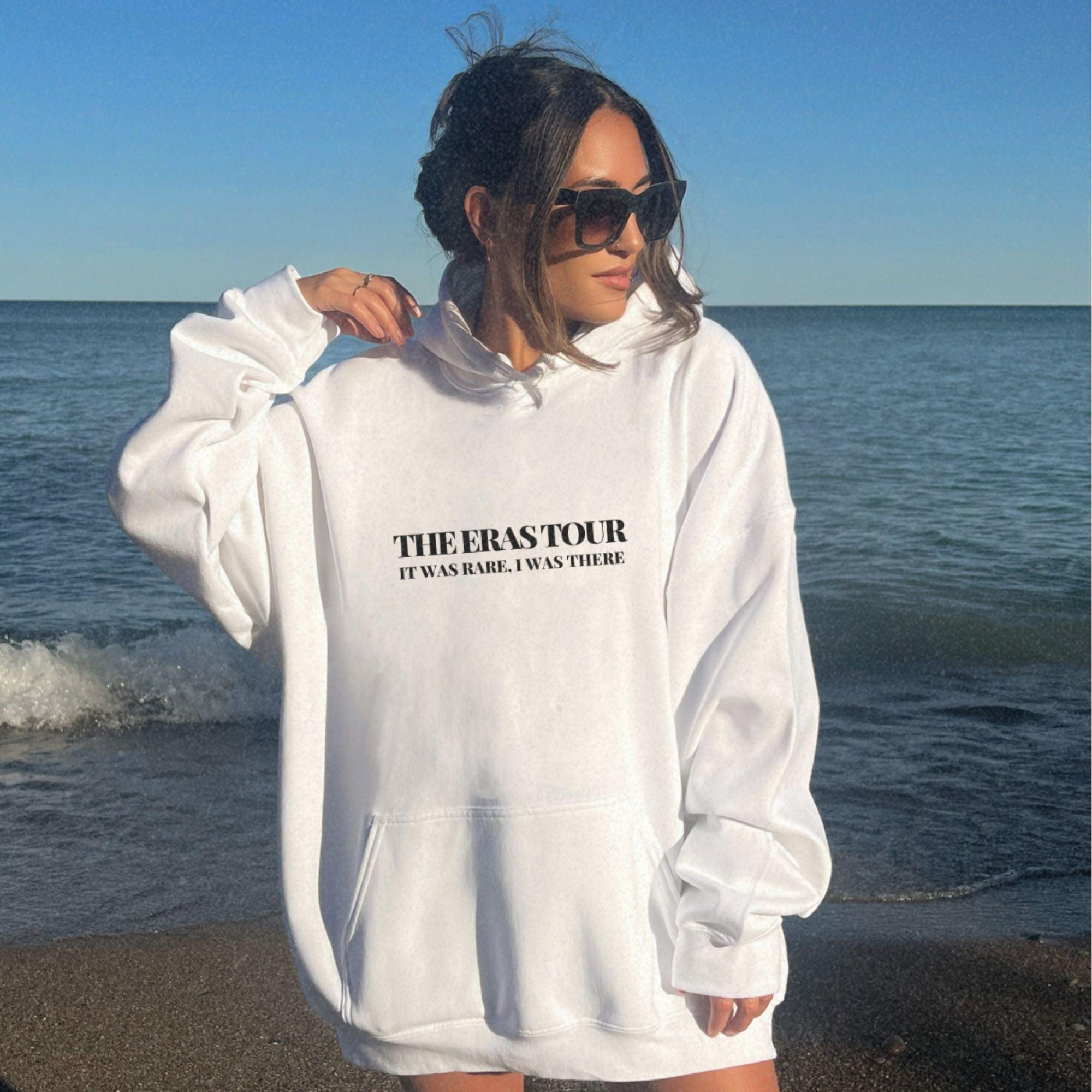 a woman standing on a beach wearing a white sweatshirt