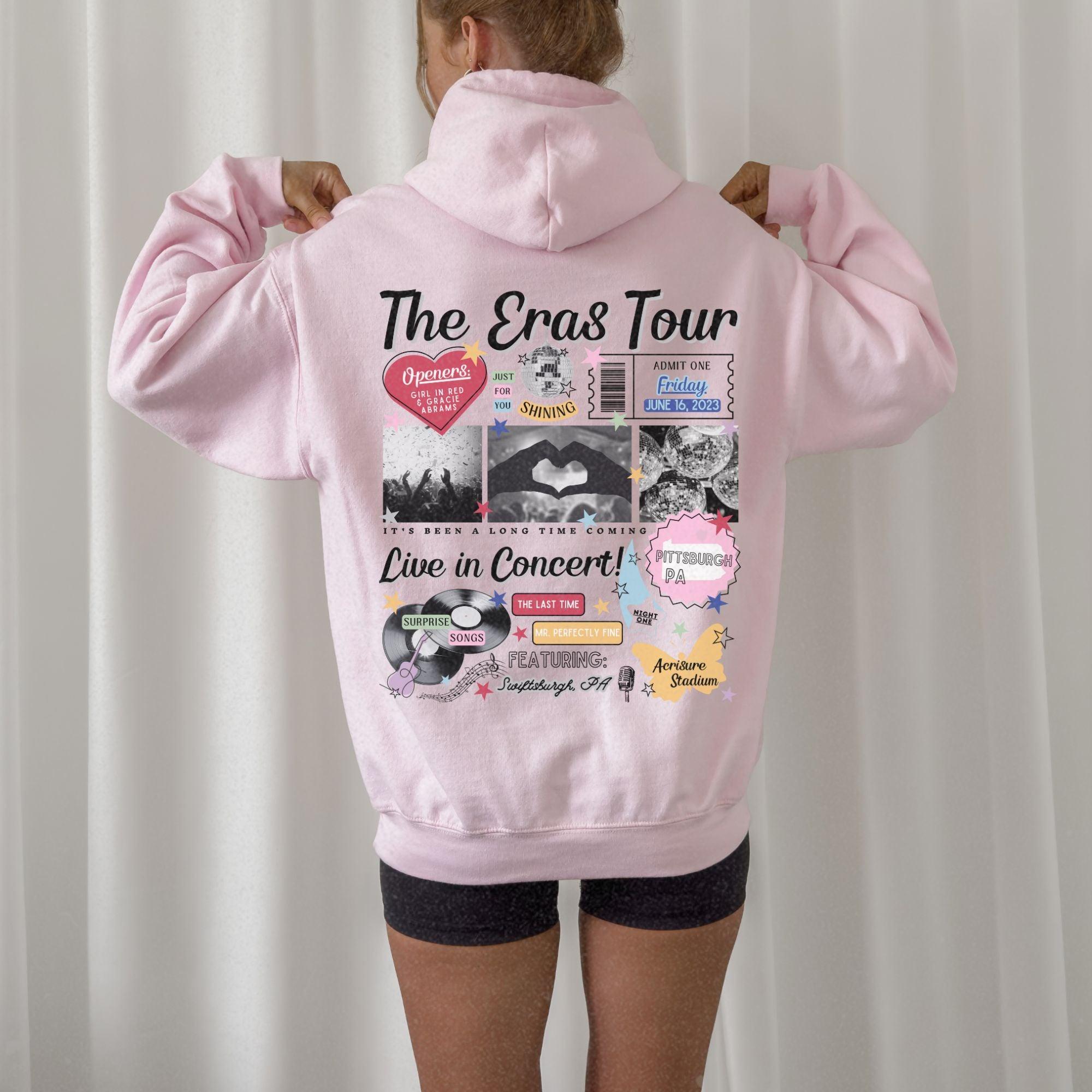 a woman wearing a pink hoodie with the words the eras tour on it