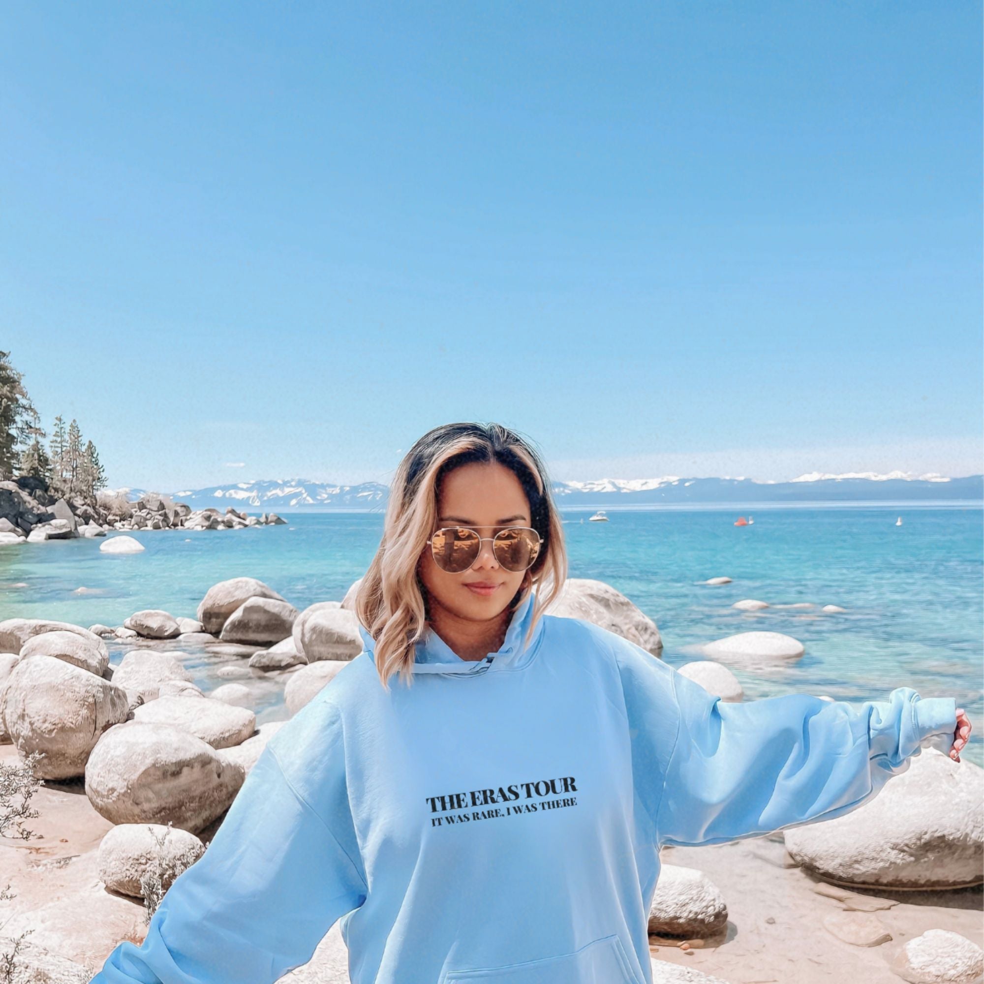 a woman in a blue sweatshirt standing on a rocky beach