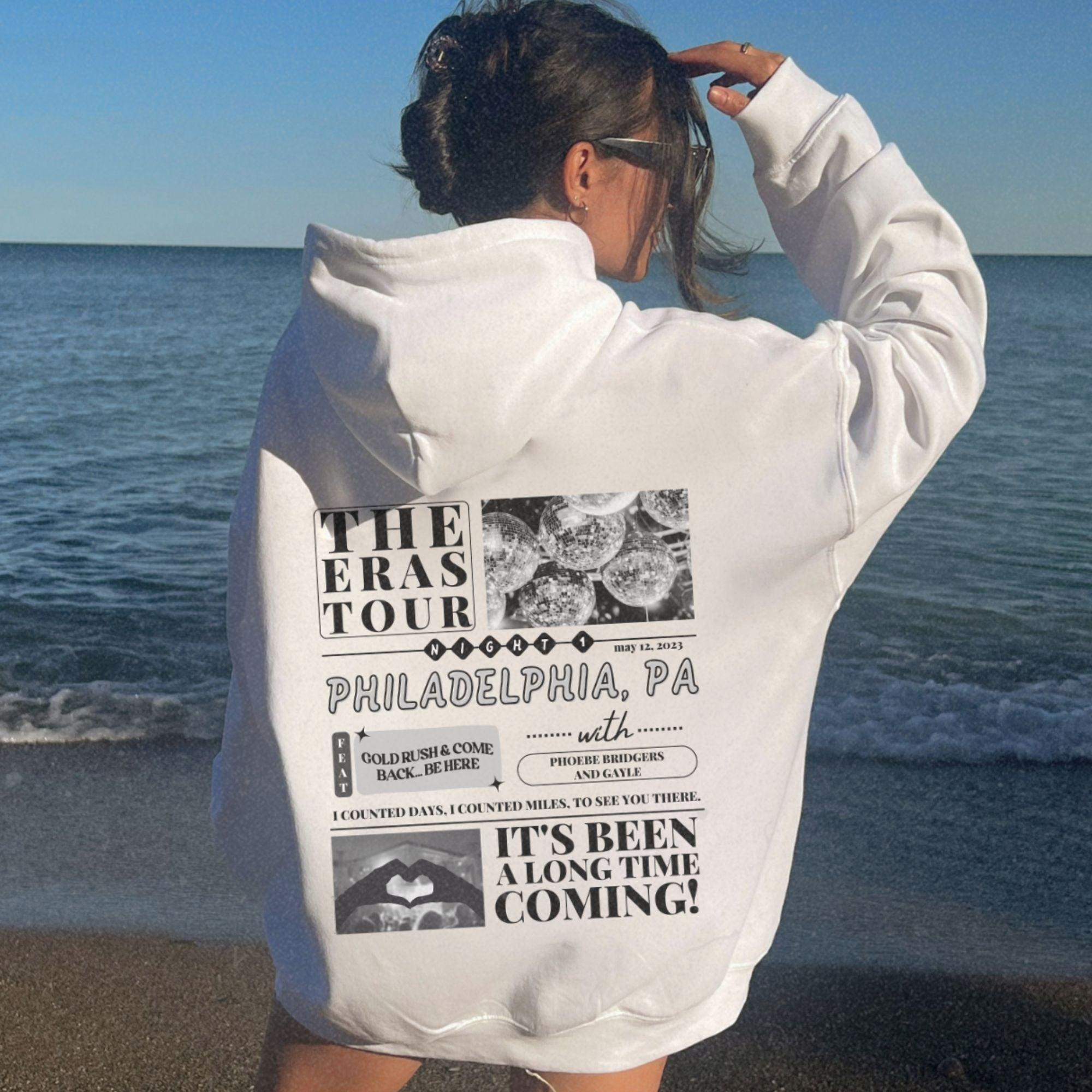 a woman standing on a beach wearing a white sweatshirt