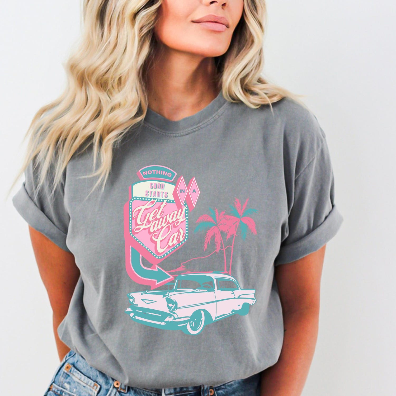 A woman wearing a gray t-shirt with a graphic design featuring a vintage car and palm trees.